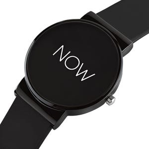 May include: A black wristwatch with a round face. The watch face displays the word "NOW" in white. The watch has a black band and a silver-colored crown.