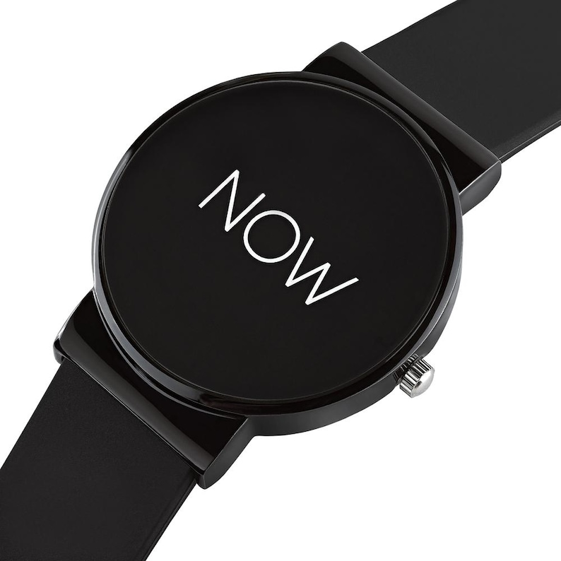 May include: A black wristwatch with a round face. The watch face displays the word "NOW" in white. The watch has a black band and a silver-colored crown.
