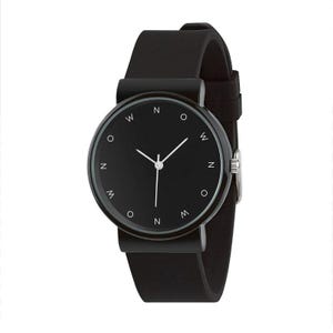 May include: A minimalist black wristwatch with a round face and a black leather strap. The watch face features white hands and small white markers at the cardinal points, with the letters "N", "W", "O", and "M" around the face.