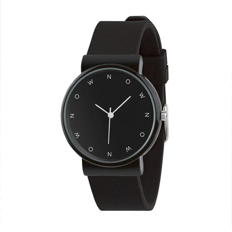 May include: A minimalist black wristwatch with a round face and a black leather strap. The watch face features white hands and small white markers at the cardinal points, with the letters "N", "W", "O", and "M" around the face.
