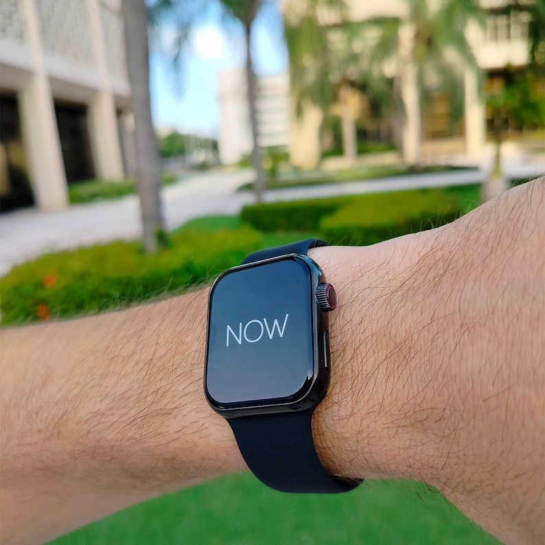 Puede incluir: Un reloj inteligente negro con una correa negra se muestra en la mu&ntilde;eca de una persona. La esfera del reloj muestra la palabra "NOW" en blanco. El reloj tiene un bot&oacute;n rojo en el lateral.