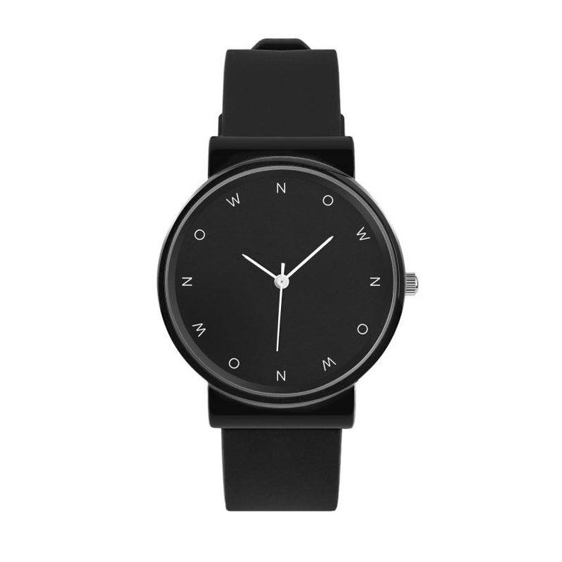 May include: A minimalist black wristwatch with a round face and a black silicone band. The watch face features white hour markers and hands. The watch has a silver crown and a simple, modern design.