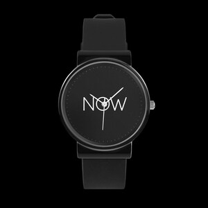 Puede incluir: Reloj de pulsera negro con esfera redonda. La esfera muestra la palabra "NOW" en blanco, con manecillas blancas que indican la hora. El reloj tiene una correa negra y una corona plateada. El fondo es negro liso.
