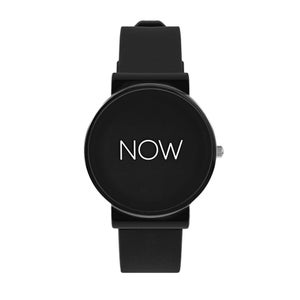 May include: A black wristwatch with a round face. The watch face displays the word "NOW" in white. The watch has a black band and a silver-colored crown.