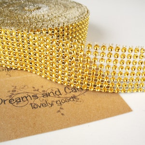 May include: A roll of gold rhinestone ribbon. The ribbon is made of small, round, gold-colored rhinestones set in a mesh backing. The text "Dreams and Cat lovely goods" is printed on a brown paper.