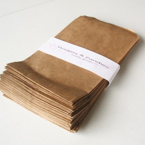 Op de afbeelding: Een stapel bruine papieren zakken met een wit label waarop "Dreams & Candies Lovely Goods" staat.