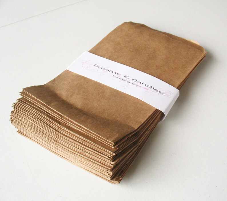 Op de afbeelding: Een stapel bruine papieren zakken met een wit label waarop "Dreams & Candies Lovely Goods" staat.
