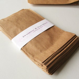 Op de afbeelding: Een stapel bruine papieren zakken met een wit label waarop "Dreams & Candles, Lovely Goods" staat.