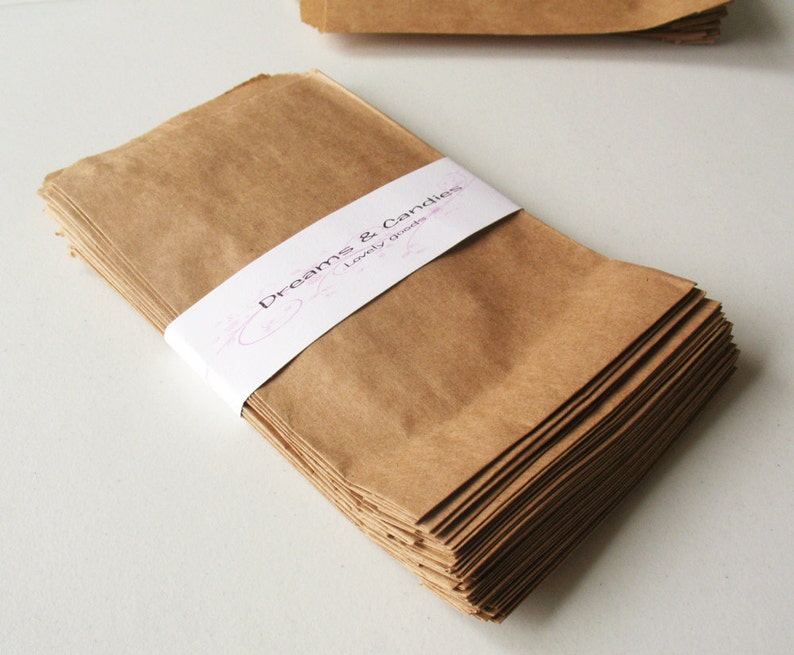 Op de afbeelding: Een stapel bruine papieren zakken met een wit label waarop "Dreams & Candles, Lovely Goods" staat.
