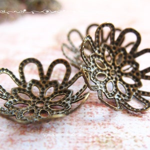 May include: Two antique gold-toned metal flower-shaped embellishments with intricate designs. The embellishments have a delicate, lacy appearance.
