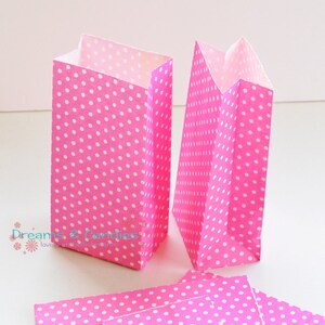 Op de afbeelding: Twee roze papieren cadeauzakjes met witte stippen. De zakjes zijn plat gevouwen en klaar om in elkaar te worden gezet.