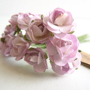 以下が含まれることがあります： 層状の花びらと緑色のワイヤーの茎を持つ、小さな薄紫色の紙の花の束。それぞれの花は柔らかいマットな質感で、繊細で丸みを帯びた花びらと、根元にある小さな緑色の萼が特徴で、それらが一つにまとめられています。