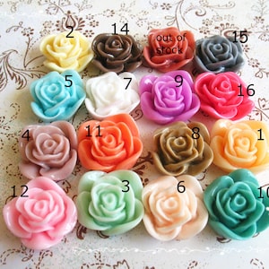 Puede incluir: Surtido de 16 cabujones de plástico en forma de rosa en varios colores, incluyendo rosa, azul, verde, naranja, marrón, blanco y amarillo. Los cabujones están dispuestos en círculo sobre un fondo blanco con los números del 1 al 16 impresos en cada cabujón.