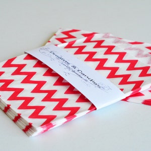 Puede incluir: Un montón de bolsas de papel con estampado de chevron rojo y blanco con una etiqueta blanca que dice "Dreams & Candies Lovely Goodies".