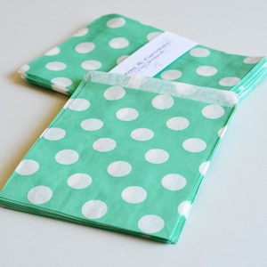 Op de afbeelding: Een stapel groene papieren cadeauzakjes met witte stippen. De zakjes zijn gevouwen en klaar voor gebruik.