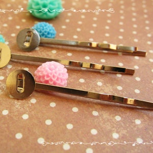 May include: Three silver-toned metal hair pins, each featuring a flat circular pad at the top with a small rectangular slot in the centre. The pins have a wavy design along the shaft and are arranged diagonally across the frame.