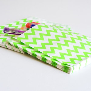 Puede incluir: Una pila de bolsas de papel con estampado de chevron verde y blanco. Las bolsas están dobladas y apiladas, con algunos bolígrafos sobresaliendo de la parte superior.