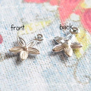 May include: Two silver-colored flower charms, one showing the front and the other the back. Each charm has five petals and a small loop at the top for attaching to jewelry. The word "front" and "back" are written above the charms.