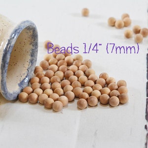 May include: A close-up of a pile of natural wood beads, spilling out of a ceramic jar. The beads are 1/4 inch (7mm) in diameter and are a light brown color. The text "Beads 1/4" (7mm)" is visible in the image.