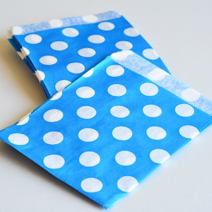 Puede incluir: Una pila de dos bolsas de papel rectangulares con un fondo azul vibrante y un patrón repetitivo de lunares blancos sólidos. Las bolsas tienen un borde superior plano y plegado, con un acabado mate y liso en un diseño sencillo y funcional.