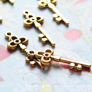 May include: A set of four gold-toned metal key charms with intricate floral designs. The keys have a vintage look and would be perfect for adding a touch of whimsy to jewelry or crafts.