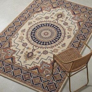 May include: Rectangular beige rug with a central medallion design in navy blue, brown, and tan. The rug features a geometric border and floral accents. A wicker chair with a gold metal frame sits beside the rug.