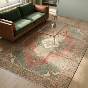 May include: A living room scene featuring a green velvet sofa with brown leather arms, a glass-top coffee table with a gold frame, and a large area rug. The rug has a red-orange background with green and cream-colored geometric patterns.