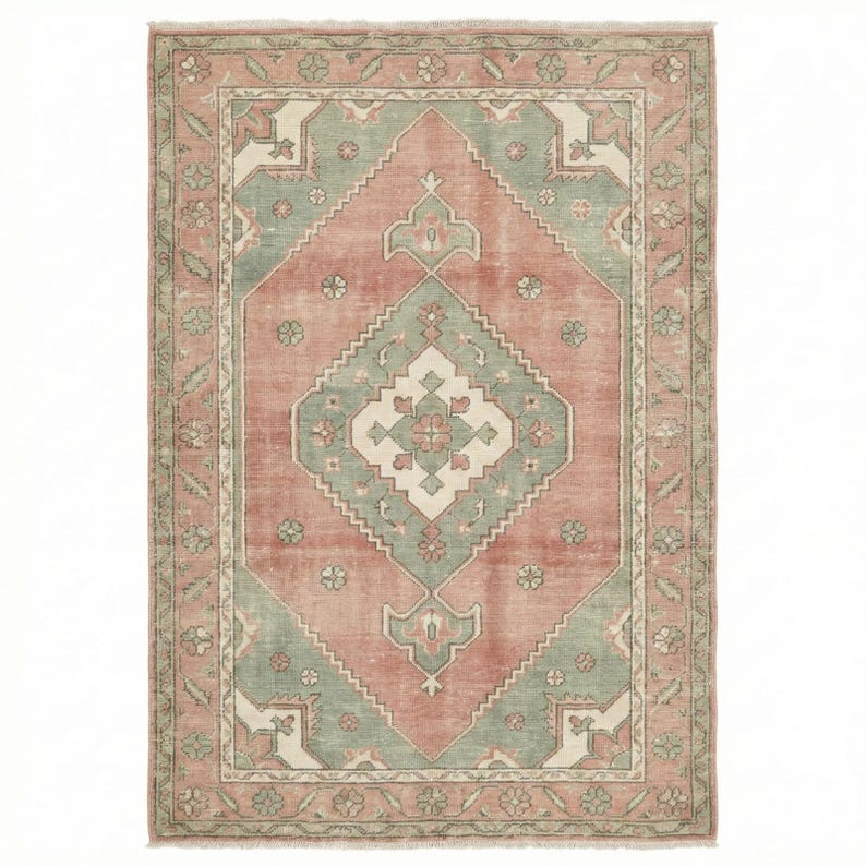 May include: A rectangular rug with a central diamond pattern in muted coral, sage green, and cream. The rug features a detailed border with floral and geometric motifs, creating a vintage or antique aesthetic. The rug's dimensions are not visible.