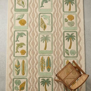 May include: A rectangular beige rug with a repeating pattern of framed images featuring seashells, dolphins, palm trees, and surfboards in shades of green, yellow, and beige. A wooden folding chair is in the bottom right corner.