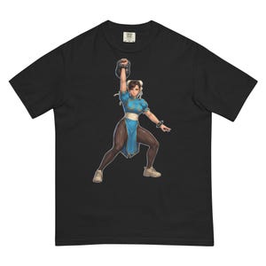 Puede incluir: Camiseta negra con un gráfico de una mujer con un vestido azul levantando una pesa rusa. La ilustración está en una pose dinámica, con la forma de la mujer enfatizada. El diseño está impreso en una camiseta cómoda e informal.
