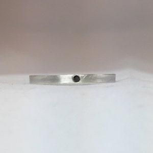 May include: A simple silver band ring with a small black gemstone in the center.