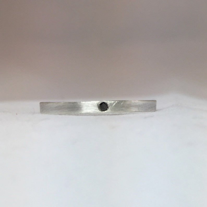 May include: A simple silver band ring with a small black gemstone in the center.