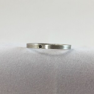 May include: A simple silver band ring with a small black diamond set in the center.