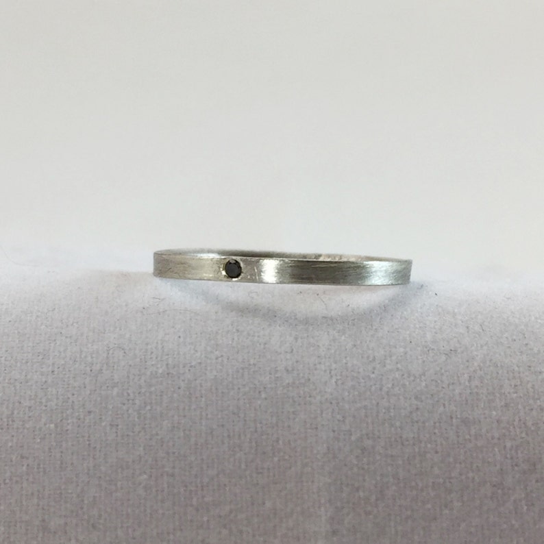 May include: A simple silver band ring with a small black diamond set in the center.
