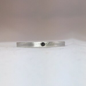 May include: A silver band with a single black diamond set in the center.