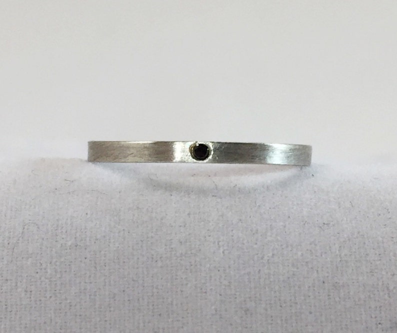 May include: A simple silver band ring with a small black gemstone in the center.