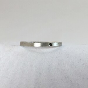 May include: A simple silver band ring with a small black gemstone set in the center.
