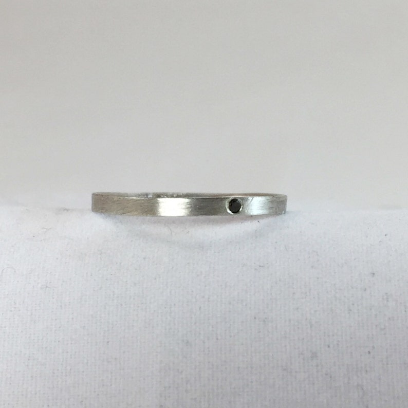 May include: A simple silver band ring with a small black gemstone set in the center.