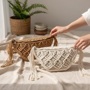 May include: Two macrame fanny packs in the image. One is tan, the other is off-white. Both have a geometric pattern, a zipper closure, and long fringe tassels. The bags are displayed on a neutral-colored surface.