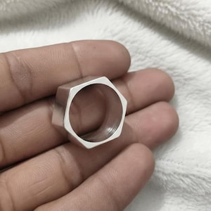 May include: A silver ring with a hexagonal shape. The ring has a hollow centre and a smooth, polished surface. This unusual ring is a piece of jewellery.