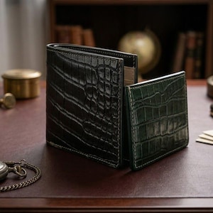 Pu&ograve; includere: Due portafogli in pelle, uno nero e uno verde, con una trama a pelle di coccodrillo, sono su una scrivania di legno. Un orologio da tasca, gemelli e penne sono anche sulla scrivania. I portafogli sono un accessorio classico.