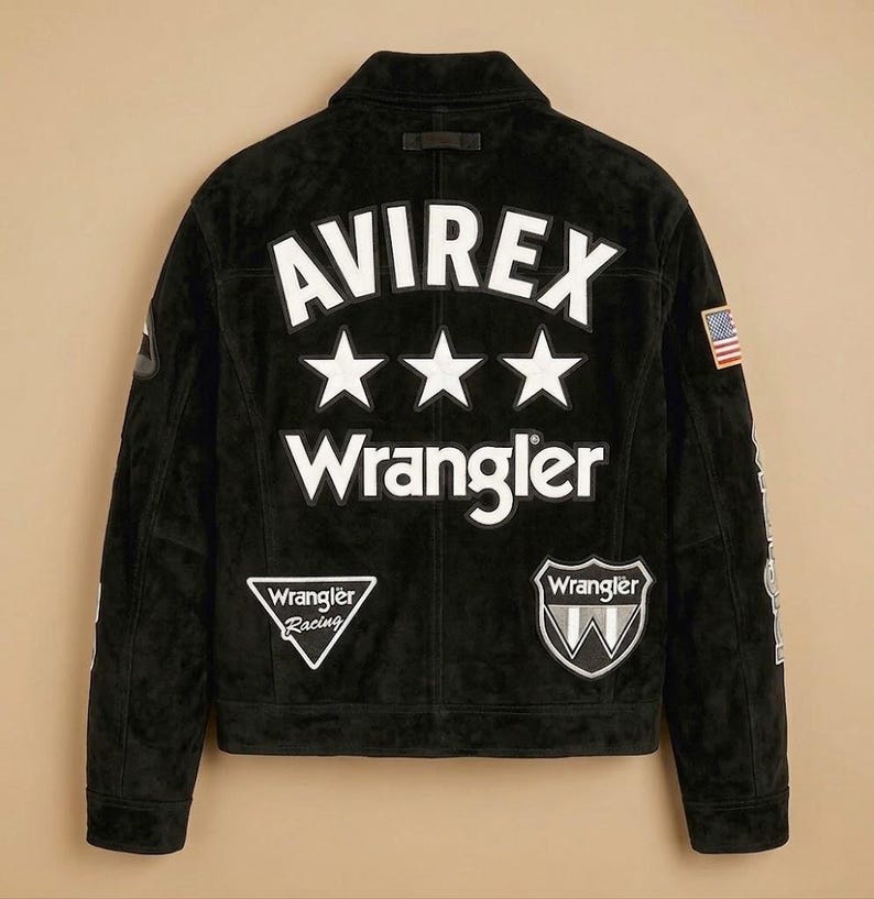 May include: Black suede jacket with the text "AVIREX" above three white stars and the word "Wrangler". Features patches with the Wrangler logo and an American flag. A classic, stylish jacket.
