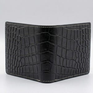 Pu&ograve; includere: Portafoglio nero a due ante con una texture in pelle di coccodrillo. Il portafoglio ha cuciture bianche sui bordi. Il portafoglio &egrave; realizzato in un materiale scuro e strutturato.