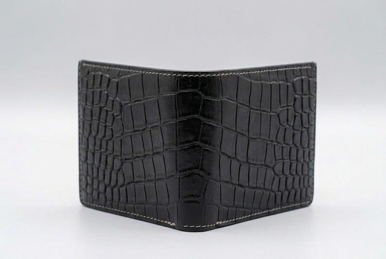 Pu&ograve; includere: Portafoglio nero a due ante con una texture in pelle di coccodrillo. Il portafoglio ha cuciture bianche sui bordi. Il portafoglio &egrave; realizzato in un materiale scuro e strutturato.