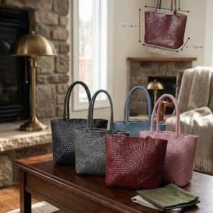 Könnte beinhalten: Eine Auswahl an gewebten Tragetaschen in verschiedenen Farben: Schwarz, Grau, Blau, Burgunderrot und Rosa. Die Taschen, ca. 41 cm breit und 28 cm hoch, stehen auf einem dunklen Holztisch und zeigen ihr strukturiertes Design und stabile Griffe.