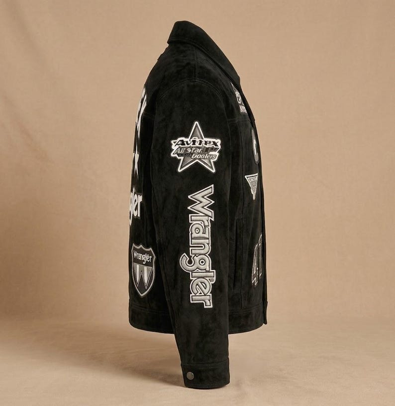 May include: Black suede jacket with white patches and the Wrangler logo. The jacket features a classic collar, buttoned cuffs, and a button closure. Patches include a star and the words "Avirex All Star Coolers".
