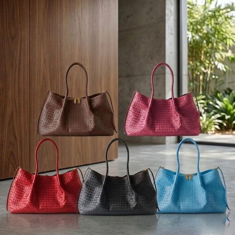 Op de afbeelding: Vijf geweven leren tote tassen in verschillende kleuren: bruin, bordeauxrood, rood, zwart en blauw. Elke tas heeft een gestructureerd ontwerp met handvatten aan de bovenkant en een goudkleurige ritssluiting. De tassen worden gepresenteerd tegen een neutrale achtergrond.