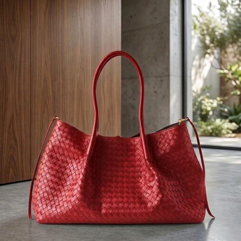 Op de afbeelding: Een rode geweven leren tote bag met lange handvatten. De tas heeft een rechthoekige vorm en een ruim interieur. De handvatten zijn gebogen en lopen omhoog. De tas is gemaakt van een geweven materiaal en heeft een gladde textuur.