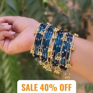 May include: A hand adorned with several blue glass bangles featuring gold-coloured embellishments and hanging charms. The bangles are a deep teal hue with an intricate design. The image also displays the text "SALE 40% OFF".