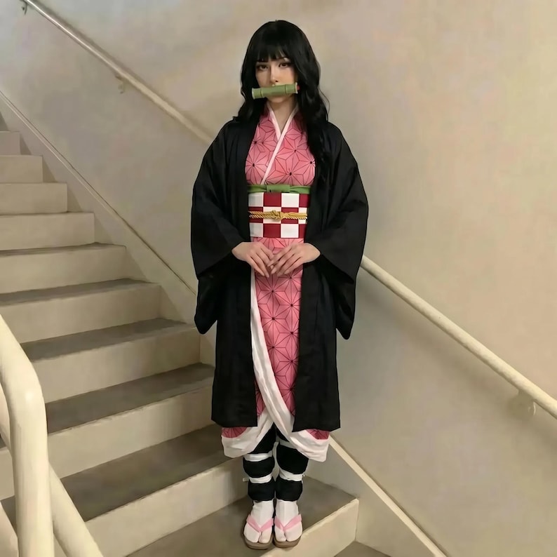 Puede incluir: Una persona con un disfraz de cosplay. El atuendo incluye un kimono negro, un kimono con estampado rosa y blanco, un obi a cuadros rojo y blanco, leggings negros y sandalias rosas. Un tubo de bamb&uacute; est&aacute; en la boca.
